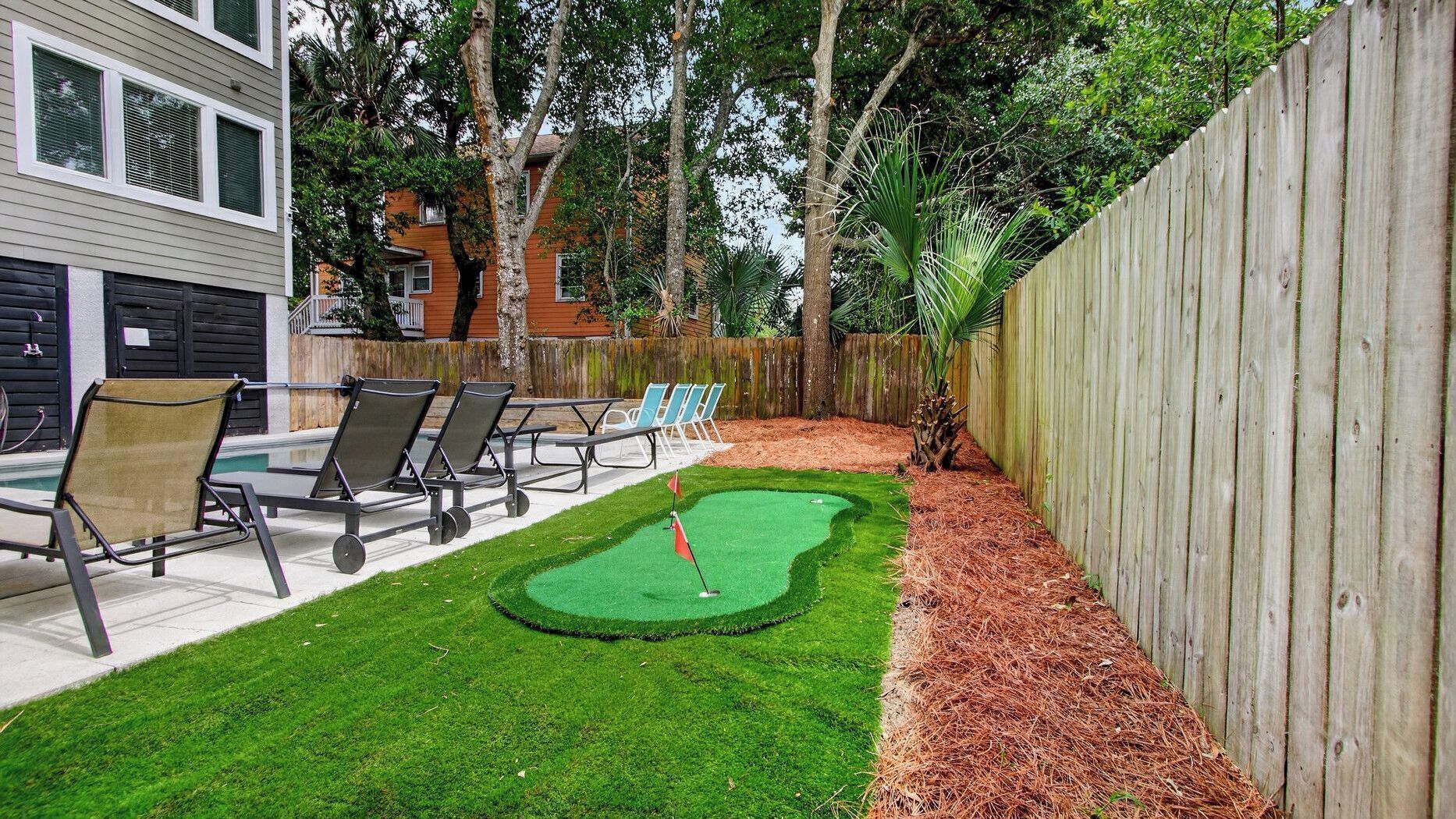 Un patio trasero con un campo de práctica de golf, sillas de descanso y una valla de madera.
