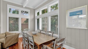 A dining area with a wooden table, white chairs, and a beige sofa. - 9 24th Avenue by Avantstay Walk to Beach + Pool + Rooftop Deck (Isle of Palms)