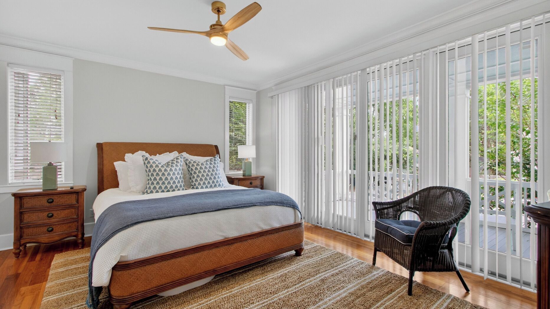 A bedroom with a bed, a nightstand, a chair, a ceiling fan, and large windows.