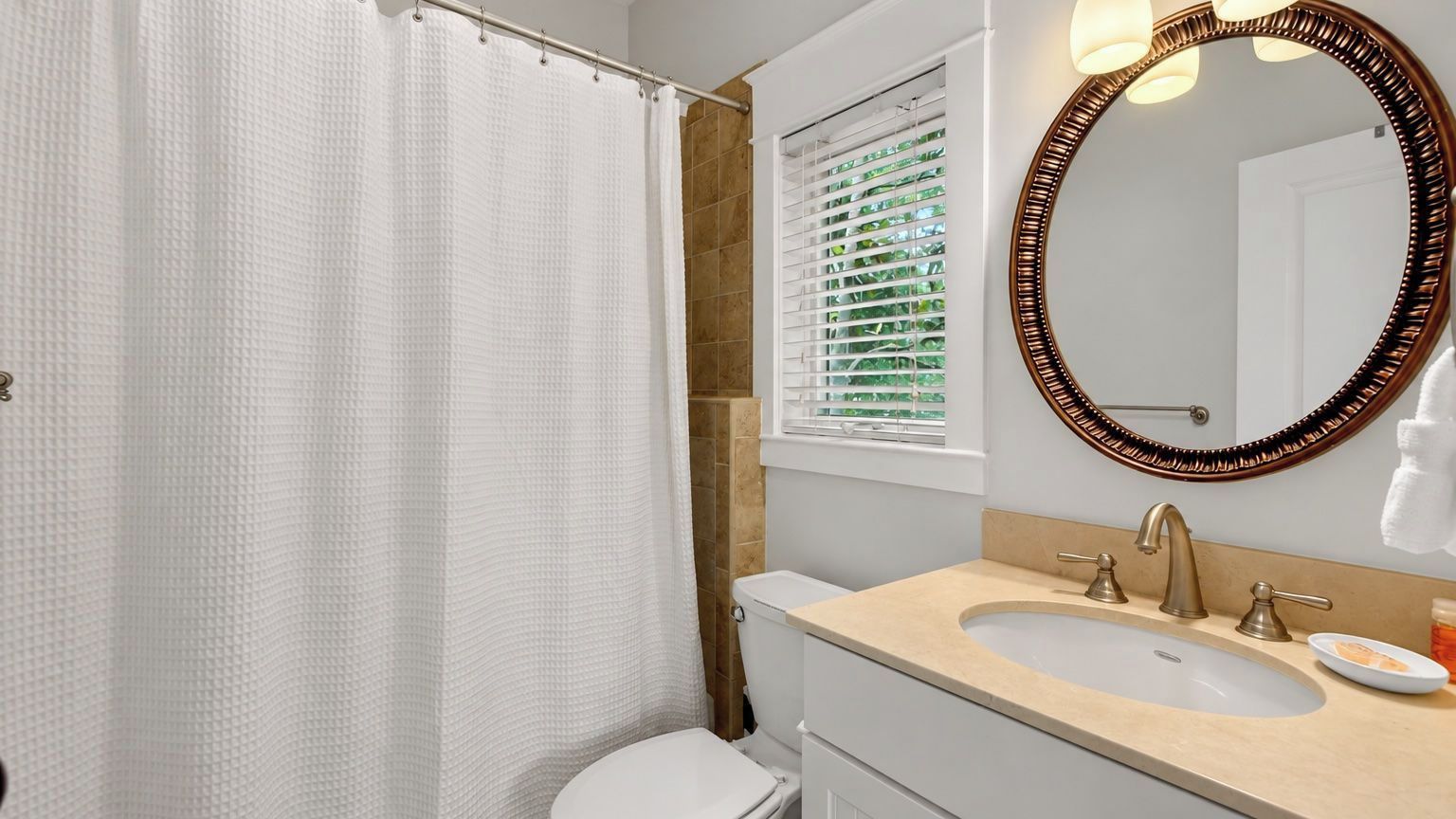 A bathroom with a shower curtain, toilet, sink, and a mirror with a decorative frame.