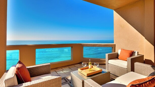 Un balcone con mobili in vimini, un tavolo con bottiglia e bicchiere e vista sull'oceano.
