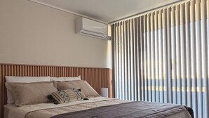 A modern hotel room with a large bed, a ceiling-mounted air conditioner, and vertical blinds on the window. - Movistar Arena Santiago Chile : Fantasilandia Concerts : Subway 10 Minutes away (Santiago)