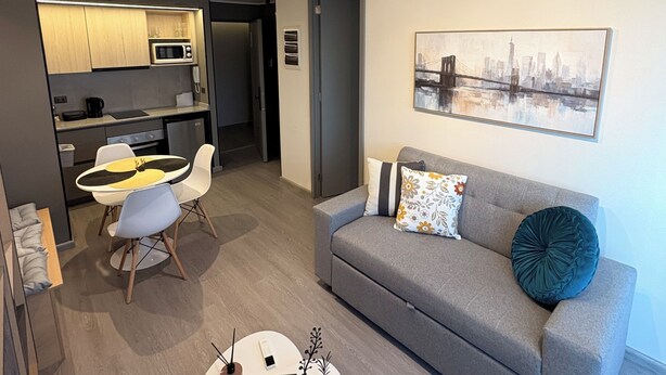 A modern living space with a kitchen, dining area, and a sofa with a cityscape painting. - Movistar Arena Santiago Chile : Fantasilandia Concerts : Subway 10 Minutes away (Santiago)