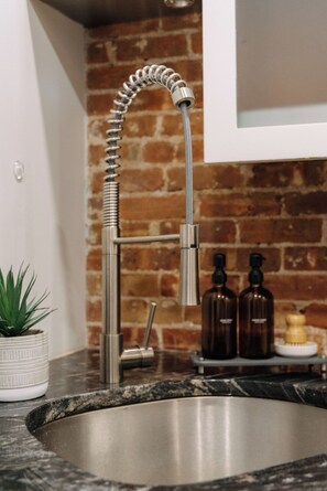 Eine Küche mit einer Edelstahl-Spüle, einem flexiblen Wasserhahn, einem Blumentopf und einer Ziegelwand.