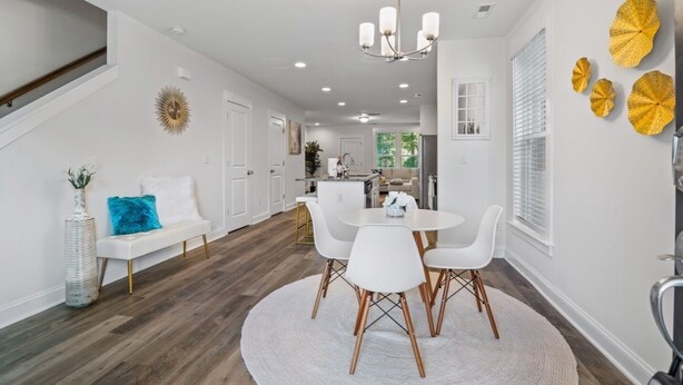 A modern kitchen with white cabinetry, a dining area with a round table and white chairs, and a staircase with a white bench.