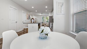 A modern kitchen with white cabinets, a central island, and a dining area with a round table.