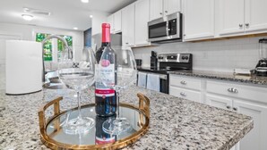 A kitchen with white cabinets, a microwave, an oven, and a wine bottle on a tray.