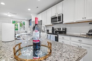 A kitchen with white cabinets, a microwave, an oven, and a wine bottle on a tray.