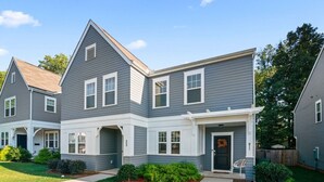 A two-story residential building with a front porch, a garage, and a well-maintained lawn.