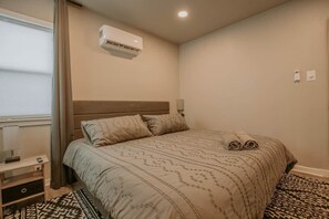 Ein Schlafzimmer mit Bett, Klimaanlage, Nachttisch und einem gemusterten Teppich.