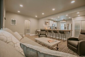 A modern living room with a sofa, coffee table, and a dining area with chairs and a kitchen in the background.