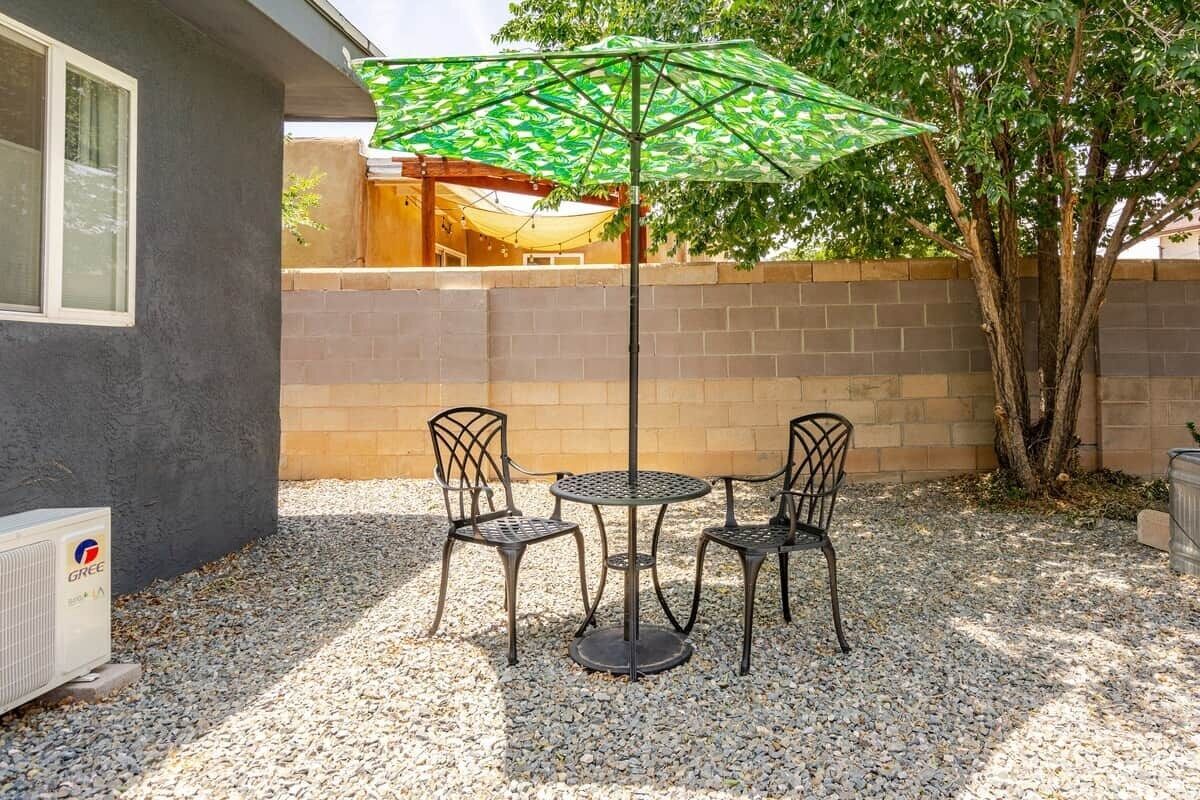 An outdoor patio with a table and chairs, a green patterned umbrella, and a brick wall.