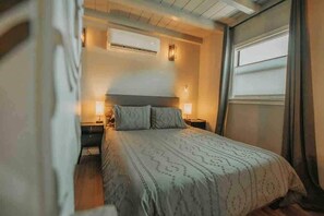 Ein Schlafzimmer mit einem Bett, zwei Nachttischen, einer Klimaanlage und einem Fenster mit Vorhängen.