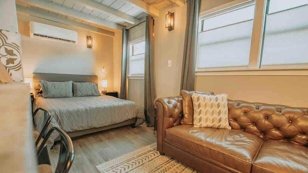 A bedroom with a bed, a leather sofa, a patterned rug, and a window with curtains. - ABQ Hub Studio - Old Town Gem! (Albuquerque)
