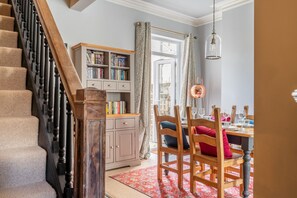 Eine Treppe mit Holzgeländer, ein Bücherregal, ein Esstisch mit Stühlen und ein Fenster mit Vorhängen.