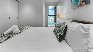 Una camera d'hotel con un letto, una finestra vista città, un quadro appeso al muro e una porta.