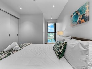 Ein Hotelzimmer mit Bett, Fenster mit Blick auf die Stadt, einem Bild an der Wand und einer Tür.