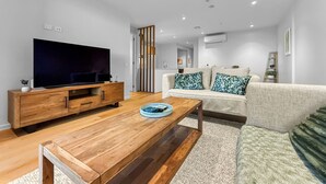 Un soggiorno moderno con una TV a schermo piatto, un tavolino in legno e un divano con cuscini decorati.