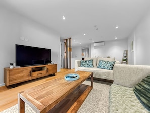 A modern living room with a flat-screen TV, wooden coffee table, and a sofa with patterned cushions. - Onehunga Luxury l New 2-Bed Apt. l Stunning Views (Auckland)