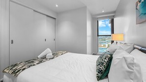 Habitación de hotel con cama, ventana con vista a la ciudad, lámpara y puerta.