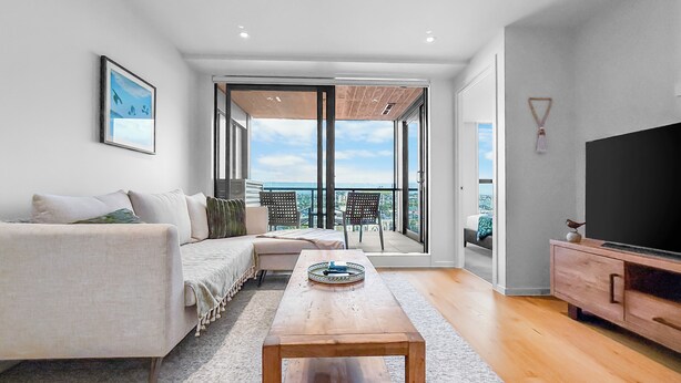 Un soggiorno moderno con un divano, un tavolino, una TV e un balcone con vista sulla città.