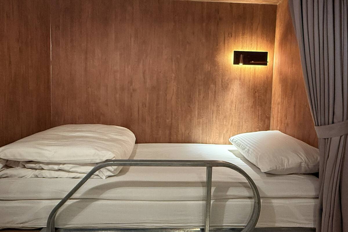 A single bed with a metal frame, a bedside table, and a wall-mounted light fixture in a room with wooden paneling.