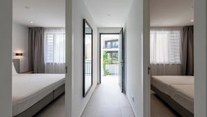 Ein Flur, der zu einem Balkon mit Blick auf ein Gebäude und Grünflächen führt.