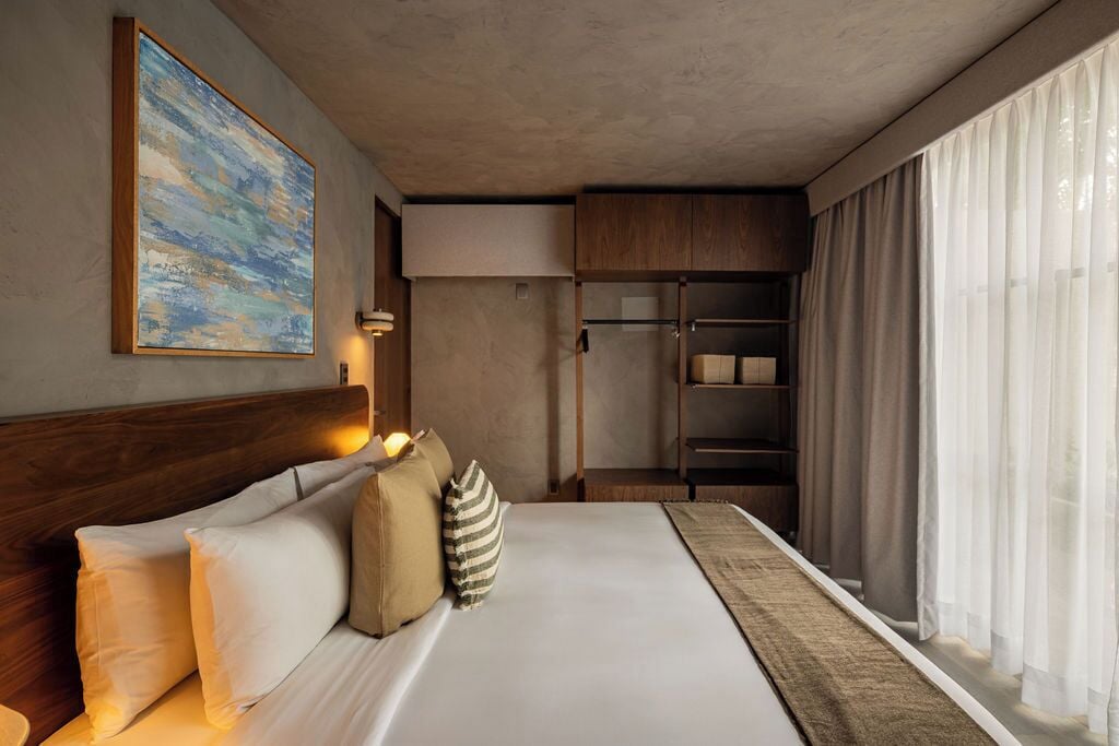 A hotel room with a bed, a painting, a wardrobe, and a window with curtains.