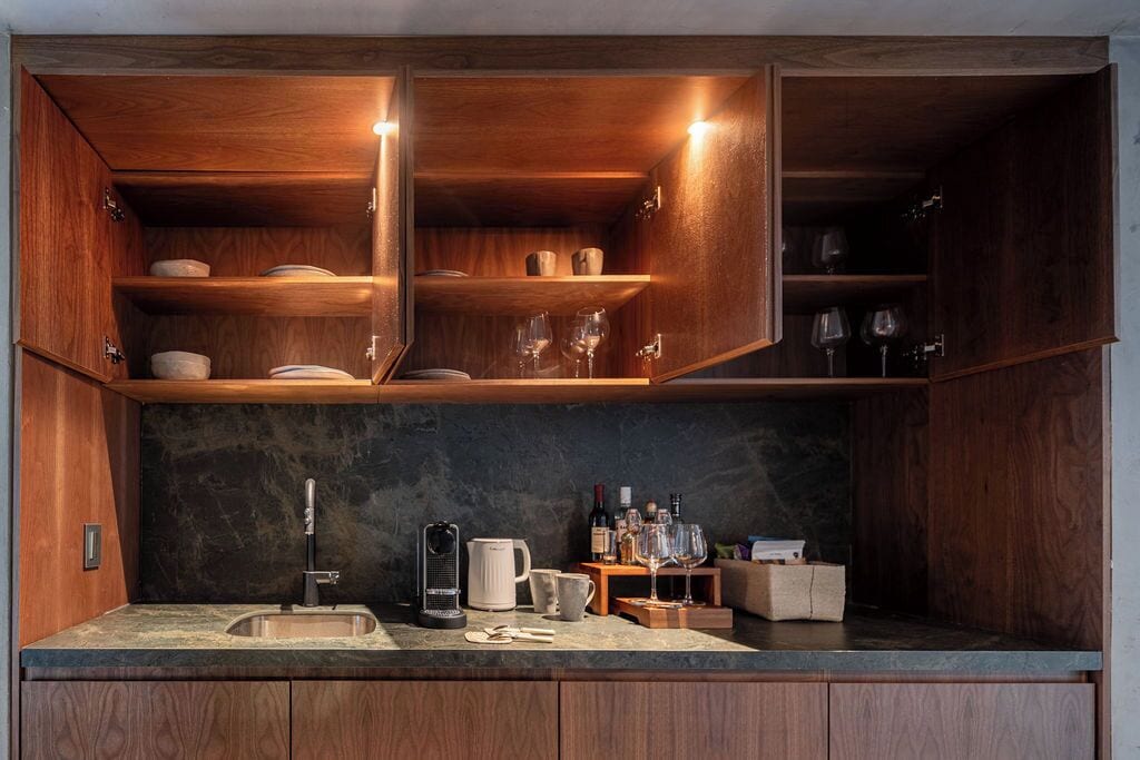 Una cocina con armarios de madera, encimera de mármol, cafetera, copas de vino y una botellaera.