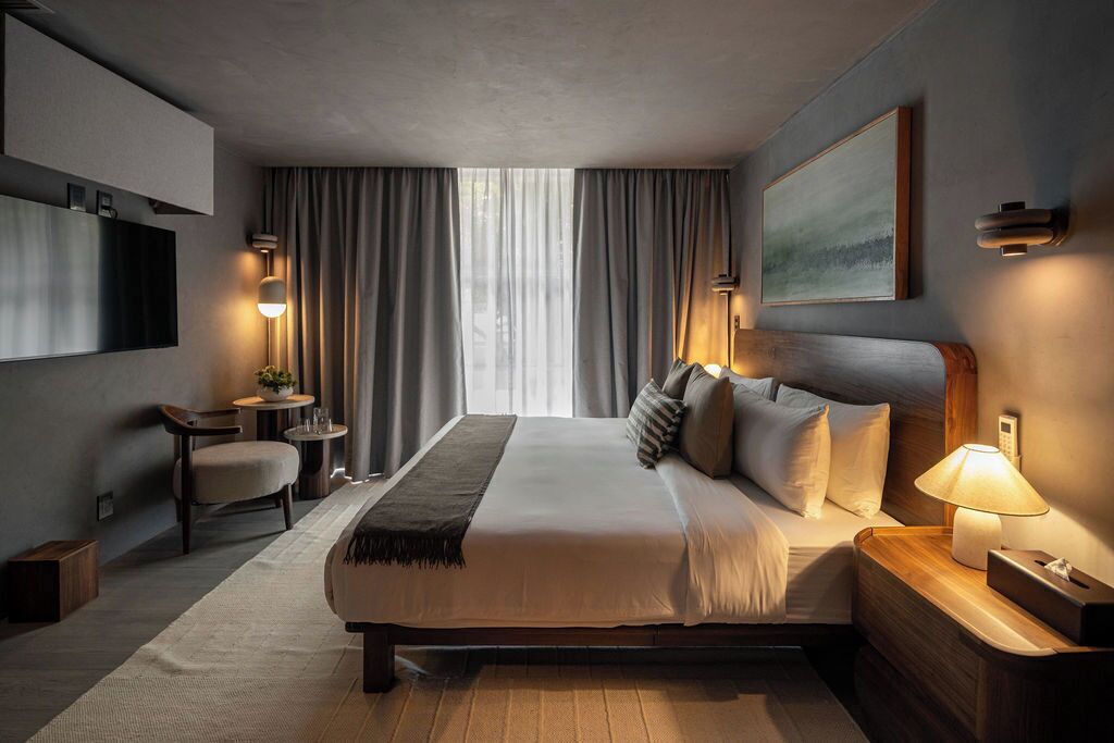 A modern hotel room with a large bed, bedside lamps, a TV, a desk, and a view of the outdoors.
