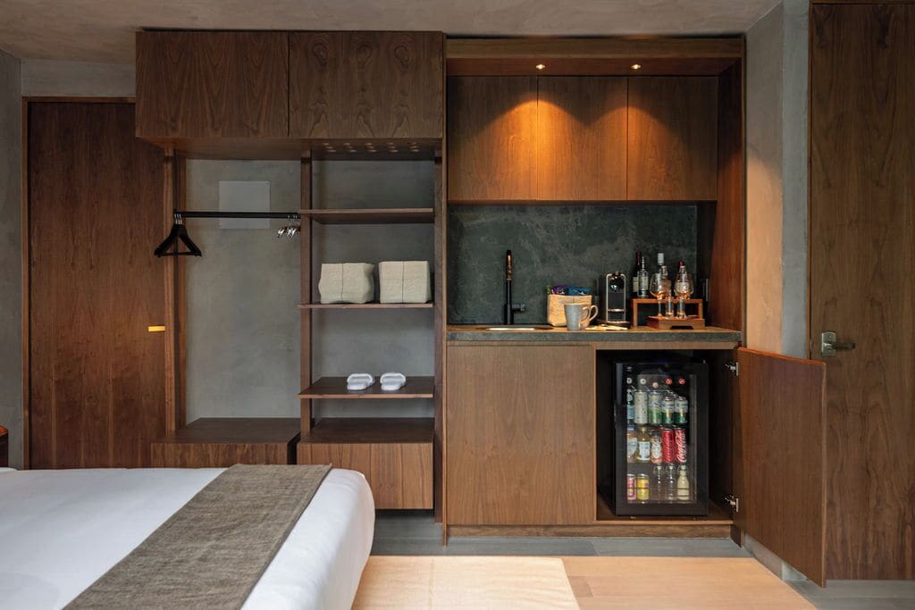 A compact hotel room with a bed, a built-in wardrobe, a small kitchenette, and a mini-fridge.