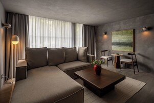 Una sala de estar moderna con un sofá seccional, una mesa de centro, una mesita auxiliar, una lámpara, un cuadro y vistas al exterior.