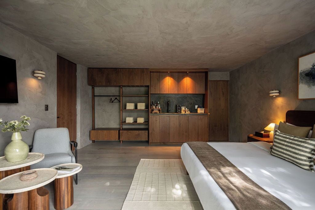 A modern bedroom with a large bed, a seating area with a table, and a built-in wardrobe.
