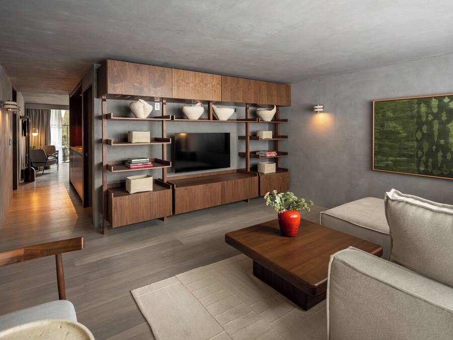 A modern living room with a flat-screen TV, wooden shelving, a red vase, and a beige sofa.