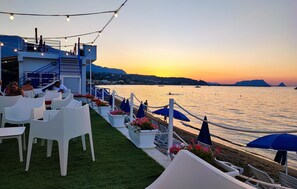 Een restaurant aan de kust met terras, uitzicht op zee en een gebouw met een blauwe gevel.