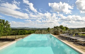 A rectangular swimming pool with a stone border, surrounded by a metal fence. There are lounge chairs aligned along the poolside. - Lovely home in Monte Santa Maria Tibe (Monte Santa Maria Tibe)