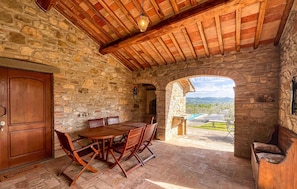A stone-walled room with a wooden ceiling, a round table with chairs, and a view of a pool and landscape. - Lovely home in Monte Santa Maria Tibe (Monte Santa Maria Tibe)