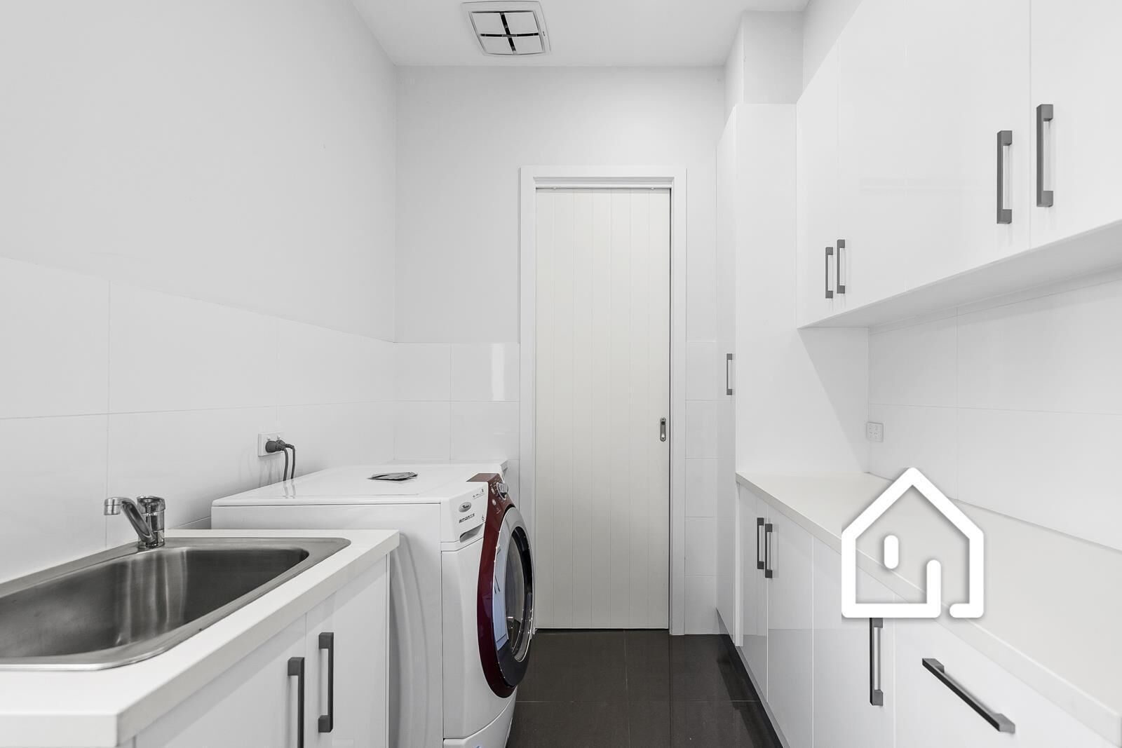 A narrow laundry room with a washing machine, a sink, and white cabinets.