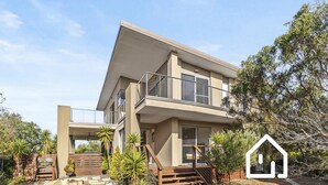Una moderna casa a due piani con un balcone, una scalinata e un giardino.