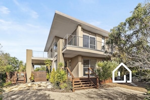 Une maison moderne à deux étages, dotée d’un balcon, d’un escalier et d’un jardin.