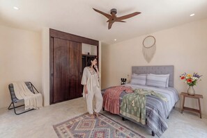 A bedroom with a bed, a ceiling fan, a wardrobe, a chair, and a bedside table with a vase of flowers. - Talulah Living 3BR Apt - Private & Shared Pool (Tulum)