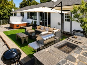 Ein Garten mit Whirlpool, Gartenmöbeln, Grill und einer Steinterrasse.