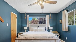 Una camera da letto con un letto, una ventola a soffitto, una finestra con tende e una porta.