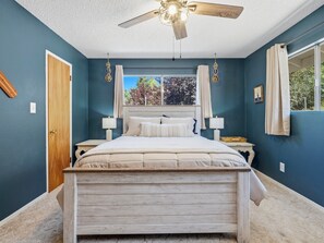 Ein Schlafzimmer mit Bett, Deckenventilator, Fenster mit Vorhängen und einer Tür.