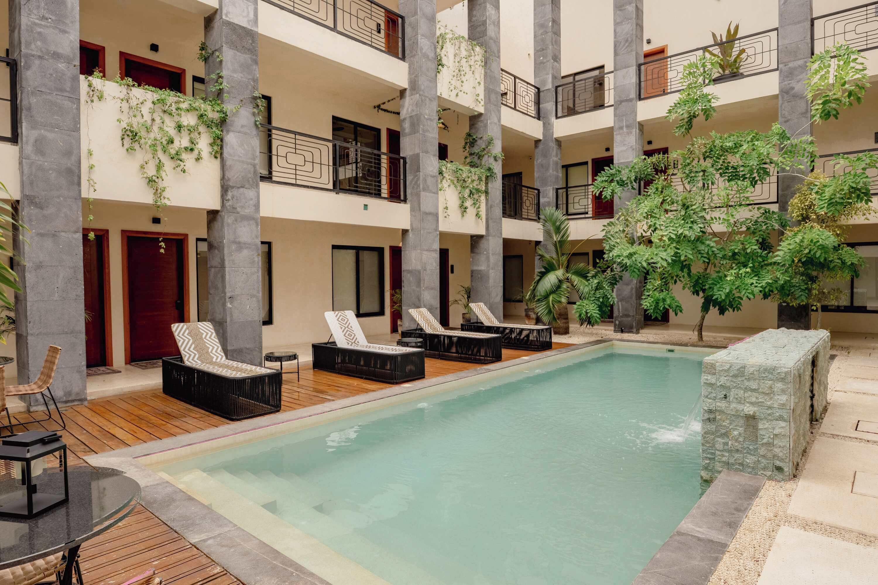 A multi-level hotel with a central pool, lounge chairs, and potted plants.