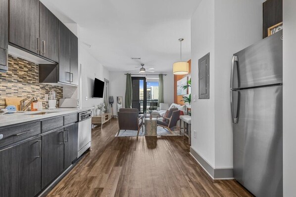 A modern kitchen with dark wood cabinets, a stainless steel refrigerator, and a dining area with a table and chairs. - 5 mins to Broadway. Midtown. Pool. Gym. Downtown. (Nashville)