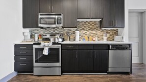 Una cocina moderna con armarios oscuros, electrodomésticos de acero inoxidable, salpicadero de azulejos y lavavajillas.