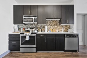 A modern kitchen with dark cabinets, stainless steel appliances, a tiled backsplash, and a dishwasher. - 5 mins to Broadway. Midtown. Pool. Gym. Downtown. (Nashville)