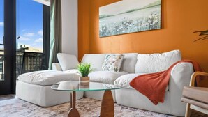 Una sala de estar con un sofá blanco, una mesa de centro de vidrio, una manta roja y un cuadro en la pared.