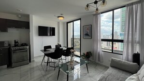 Ein modernes Wohnzimmer mit Essbereich, einer Küche inklusive Herd und Backofen, einem Flachbildfernseher und großen Fenstern mit Blick auf die Stadt.
